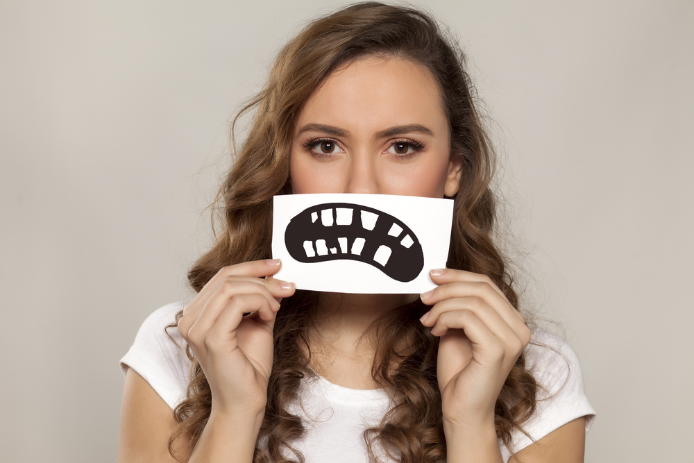 Young woman holding picture of sad mouth with missing teeth